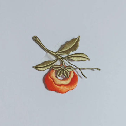 Chanhua handmade persimmon brooch with orange fruit, olive-green branch, multiple leaves, and bare twig tips, displayed on a light gray background