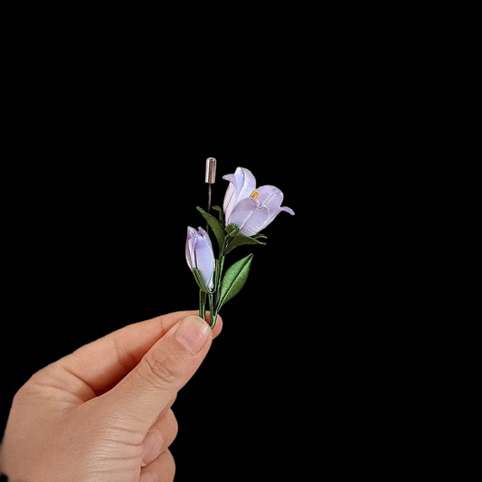 Close-up of Chanhua bellflower brooch showing thread-wrapped lavender petals, soft yellow center, and dark green leaf detail