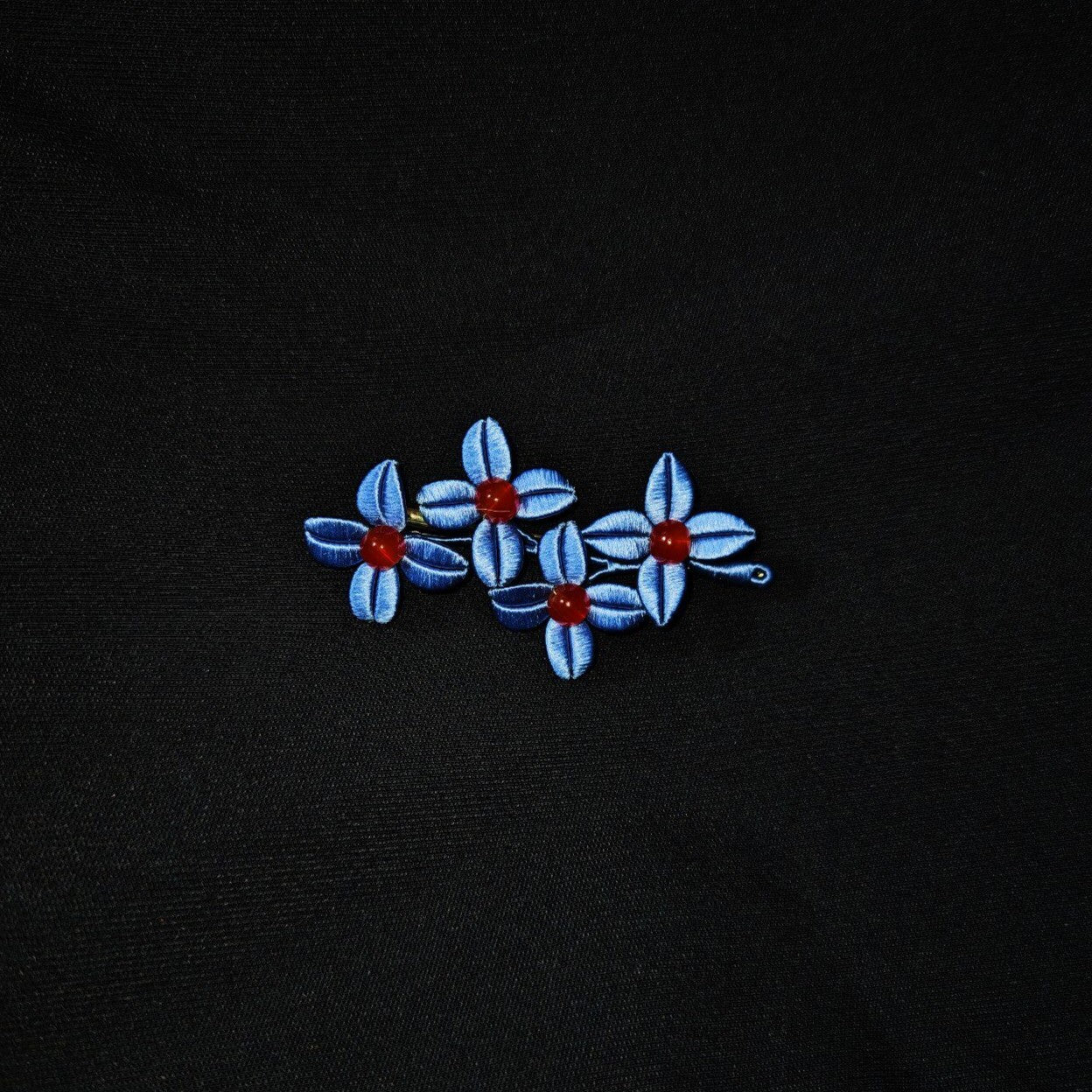 Chanhua Weiyang handmade blue flower brooch with three small four-petal flowers and deep red bead centers, worn on a black jacket