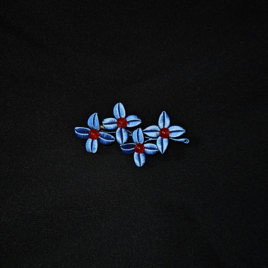 Chanhua Weiyang handmade blue flower brooch with three small four-petal flowers and deep red bead centers, worn on a black jacket