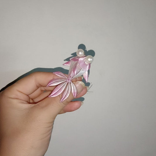 Handmade Chanhua pink ombre goldfish brooch with layered fin petals, broad fan tail, and two pearl eyes, held in hand against a grey background