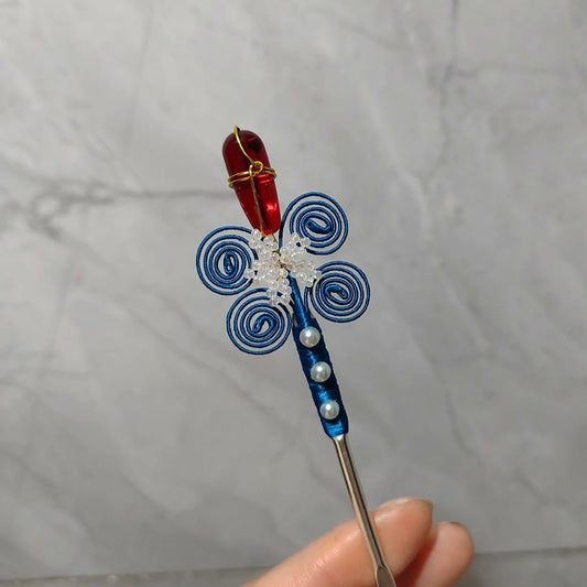 Handheld view of a handcrafted Chanhua thread-wrapped hairpin featuring a red flower bud and blue spiral patterns with pearl accents.