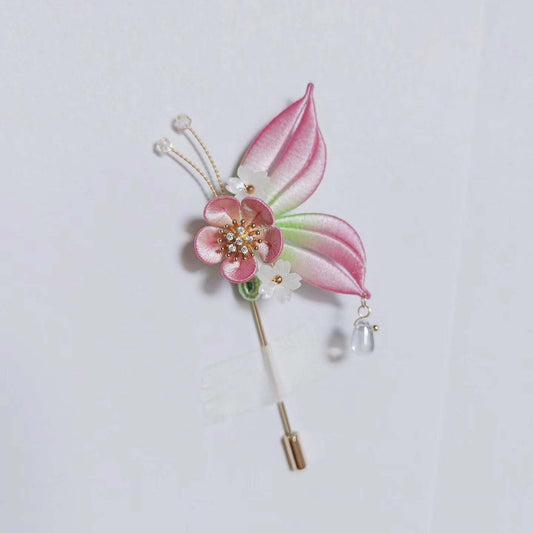 Chanhua handmade butterfly brooch with pink ombre wings, plum blossom body, gold antenna with crystal tips, and clear crystal drop pendant, displayed on a light gray background