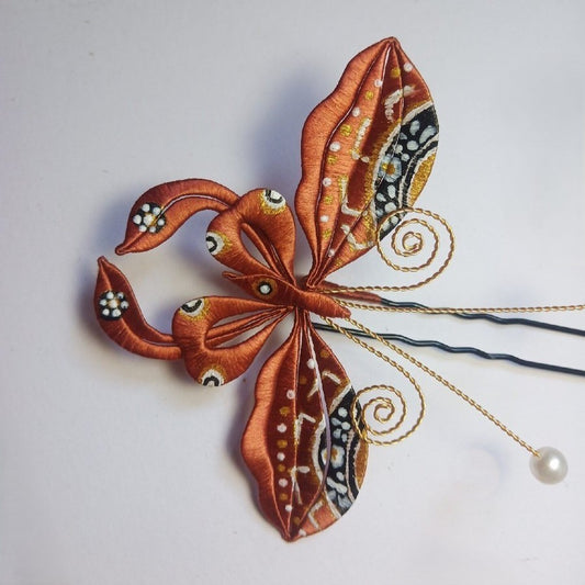 3D artisanal hairpin with orange and brown thread-wrapped wings, golden wire spirals, and pearl accents.