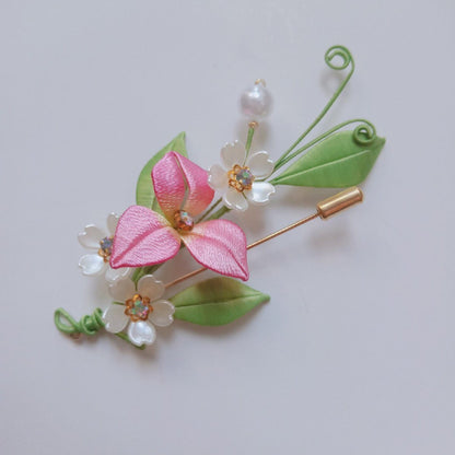 3D floral pin depicting a soft pink blossom made with intricate artisanal thread-wrapping techniques.