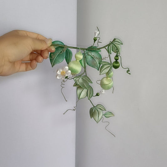 Handcrafted Chanhua gourd vine decor featuring thread-wrapped green gourds, white flowers, and leaves held in a hand.