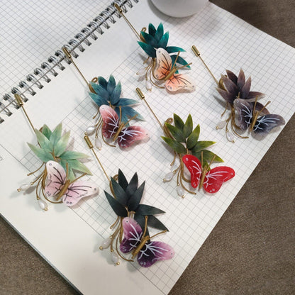 Ronghua handmade bamboo and butterfly brooches in six color combinations, each with velvet silk butterfly, pointed bamboo leaves, pearl drop, and gold stick pin, displayed on white grid paper