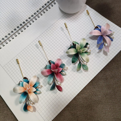 Ronghua handmade orchid brooches in four ombre color options — orange and teal, pink and teal, green and cream, and pink and blue — each with pearl sprigs on wire stems and a gold stick pin, displayed on white grid paper
