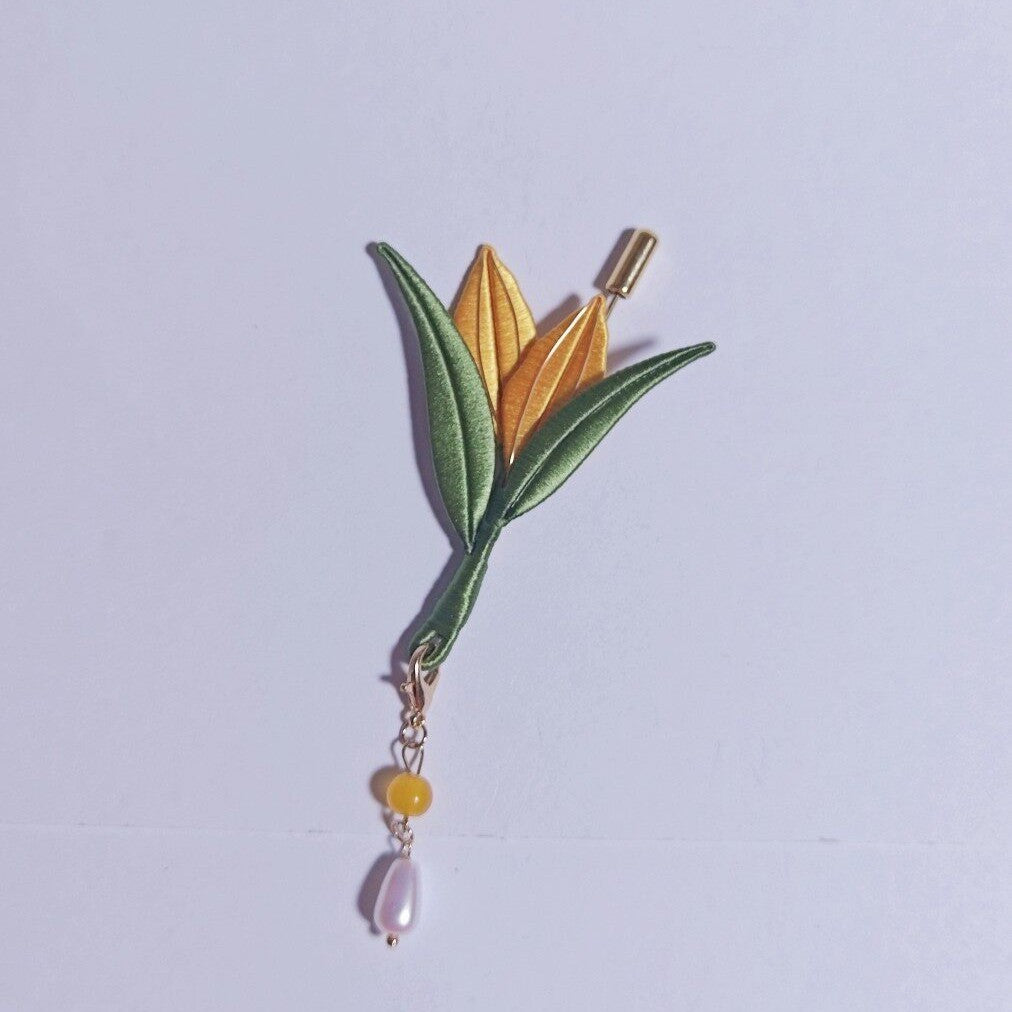 Chanhua handmade corn brooch with golden yellow bud, green leaves, and a pearl drop on a gold chain, displayed on a light gray background