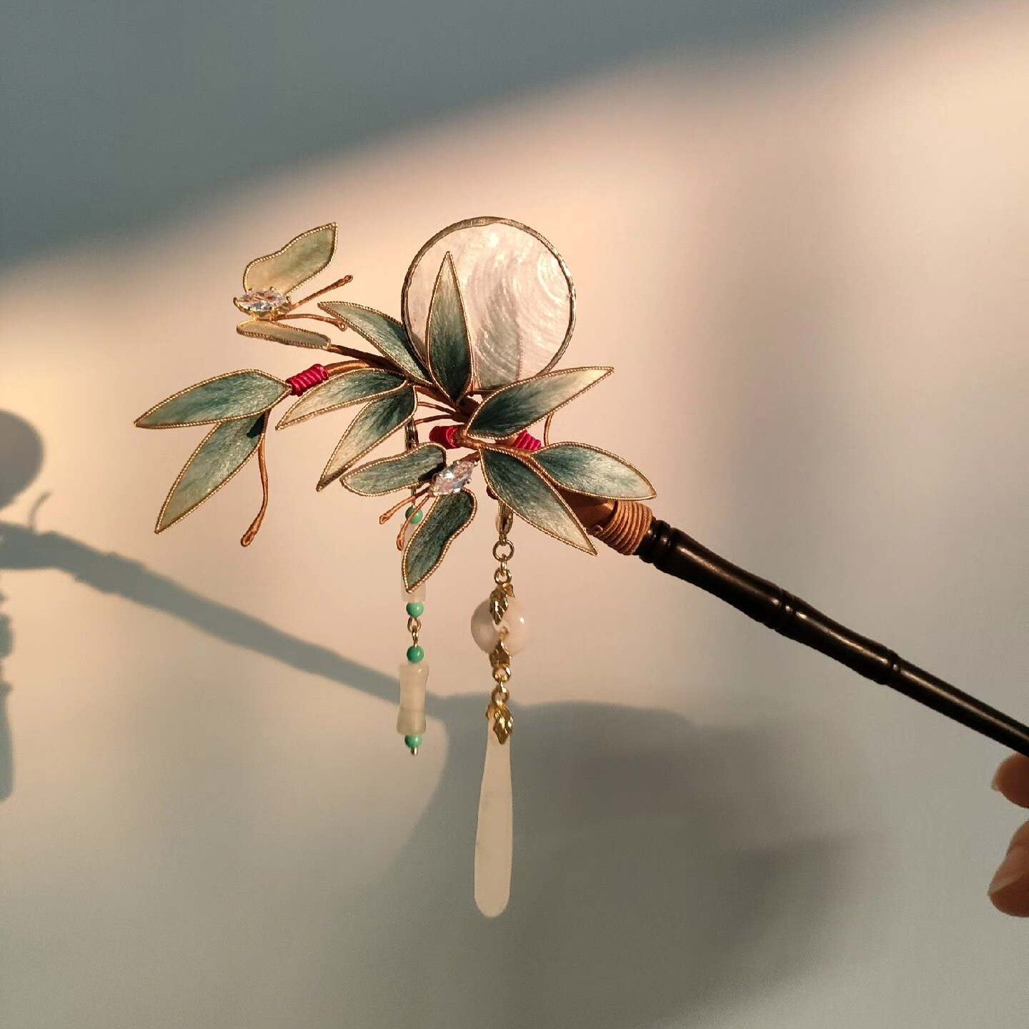 Ronghua handmade bamboo and butterfly hairpin with teal velvet leaves, gold edge trim, iridescent shell disc, crystal and jade pendants, and dark wooden pin, displayed on dark grey fabric