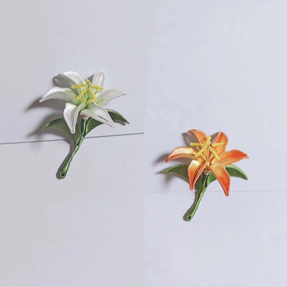 Chanhua handmade lily brooches in white and orange, each with yellow stamens and green leaves on a curved stem, displayed on a light gray background