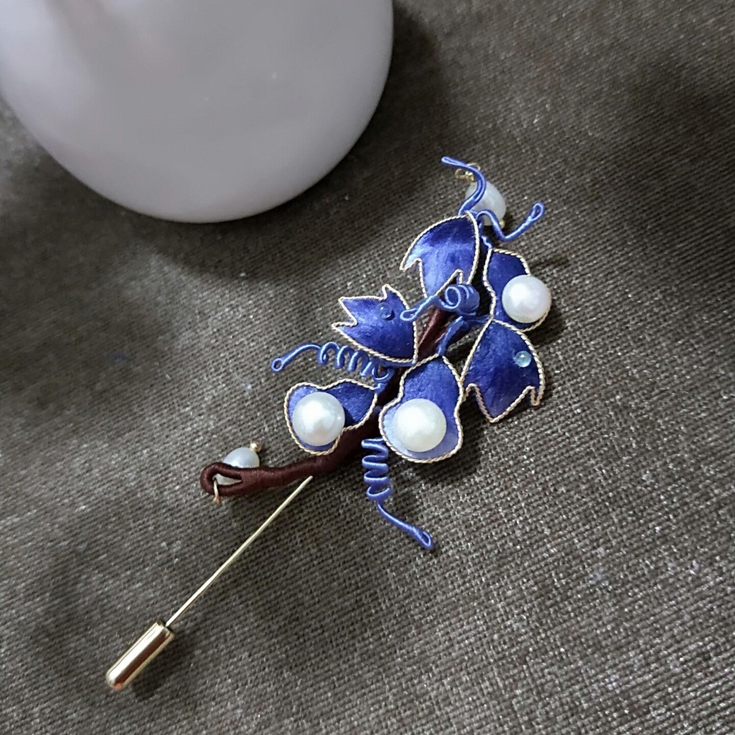 Ronghua handmade gourd brooch with blue velvet silk gourds, gold edge trim, large pearl accents, blue wire tendrils, and a gold stick pin, displayed on dark grey fabric