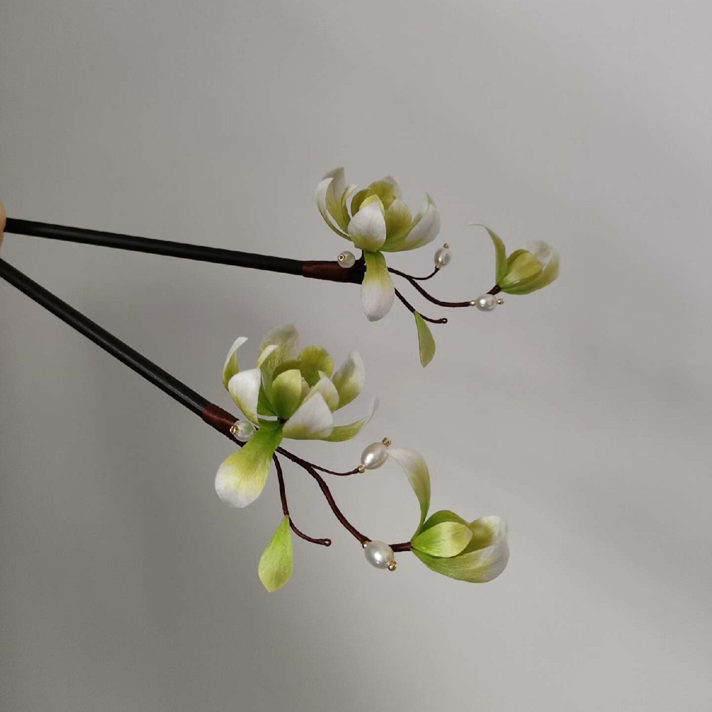Ronghua handmade magnolia hairpin with white and green silk petals, two green buds, dark brown wire branches, pearl accents, and a dark wooden pin, displayed against a light gray background