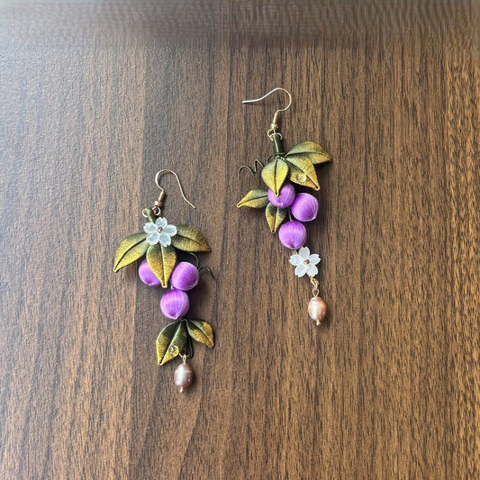 Chanhua handmade purple grape drop earrings with gold-green leaves, small white flower accent, and pink pearl drop, displayed on dark wood surface