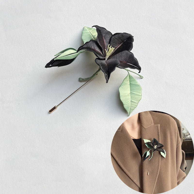 Elegant black Chanhua datura flower brooch pinned on a beige coat, featuring intricate floral details and green leaves.