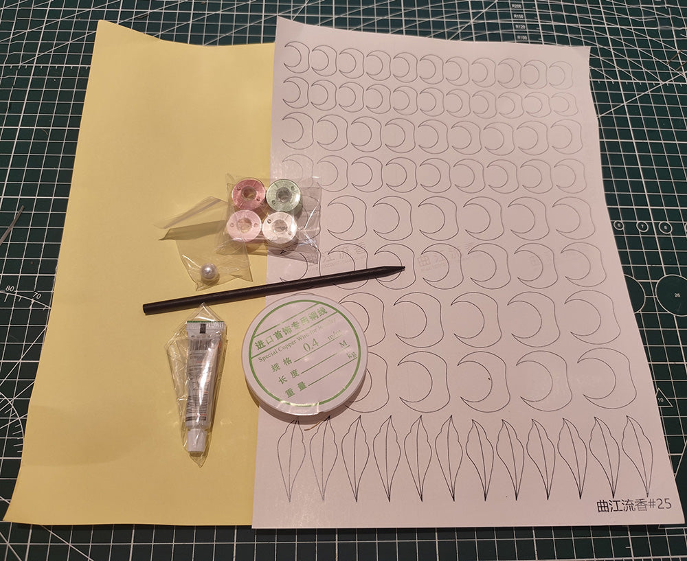 Flat lay of the Chanhua hairpin DIY kit contents, including colored silk threads, copper wire, patterns, a pearl, glue, and a hairpin stick on a craft mat.