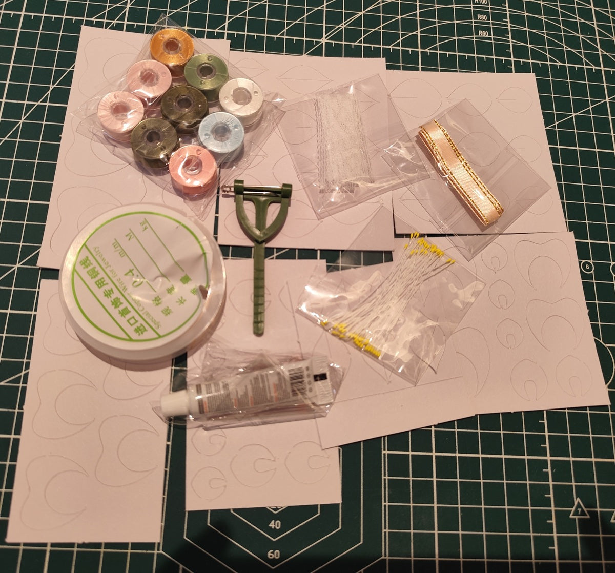DIY rose corsage craft kit materials including spools of thread, pre-cut fabric petals, floral wire, and ribbons on a green cutting mat.