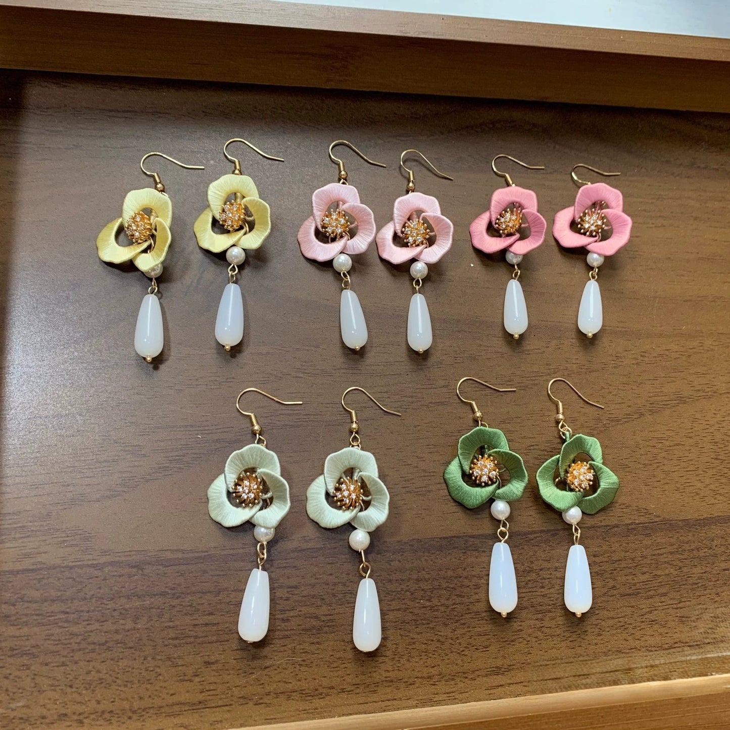 Collection of handmade Chanhua flower earrings in various soft colors on a white fabric background.