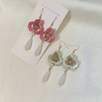 Pair of pink Chanhua flower earrings and a pair of light gray ones, displayed on a card and a white fabric background.
