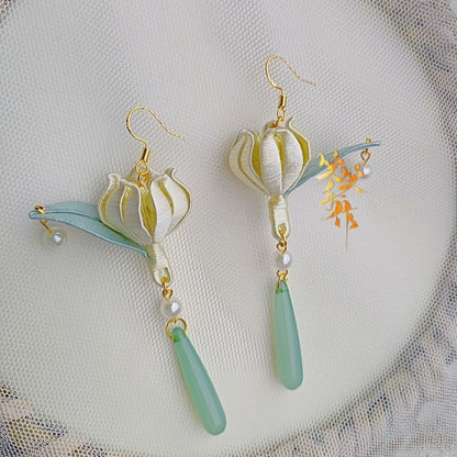 Close-up of the handcrafted Chanhua bloom earrings, showcasing intricate folded fabric petals, with 925 silver hooks and dangling freshwater pearls and green teardrop beads.