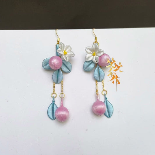 A pair of handcrafted Chanhua floral drop earrings with white flowers, light blue leaves, and pink pearl-like beads, featuring 925 silver hooks, displayed on a white surface.