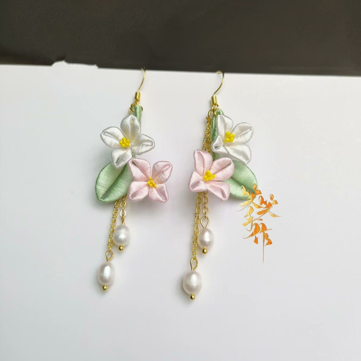 Elegant Chanhua flower dangle earrings featuring handmade white and pink silk flowers, green leaves, and natural freshwater pearls on a white background.