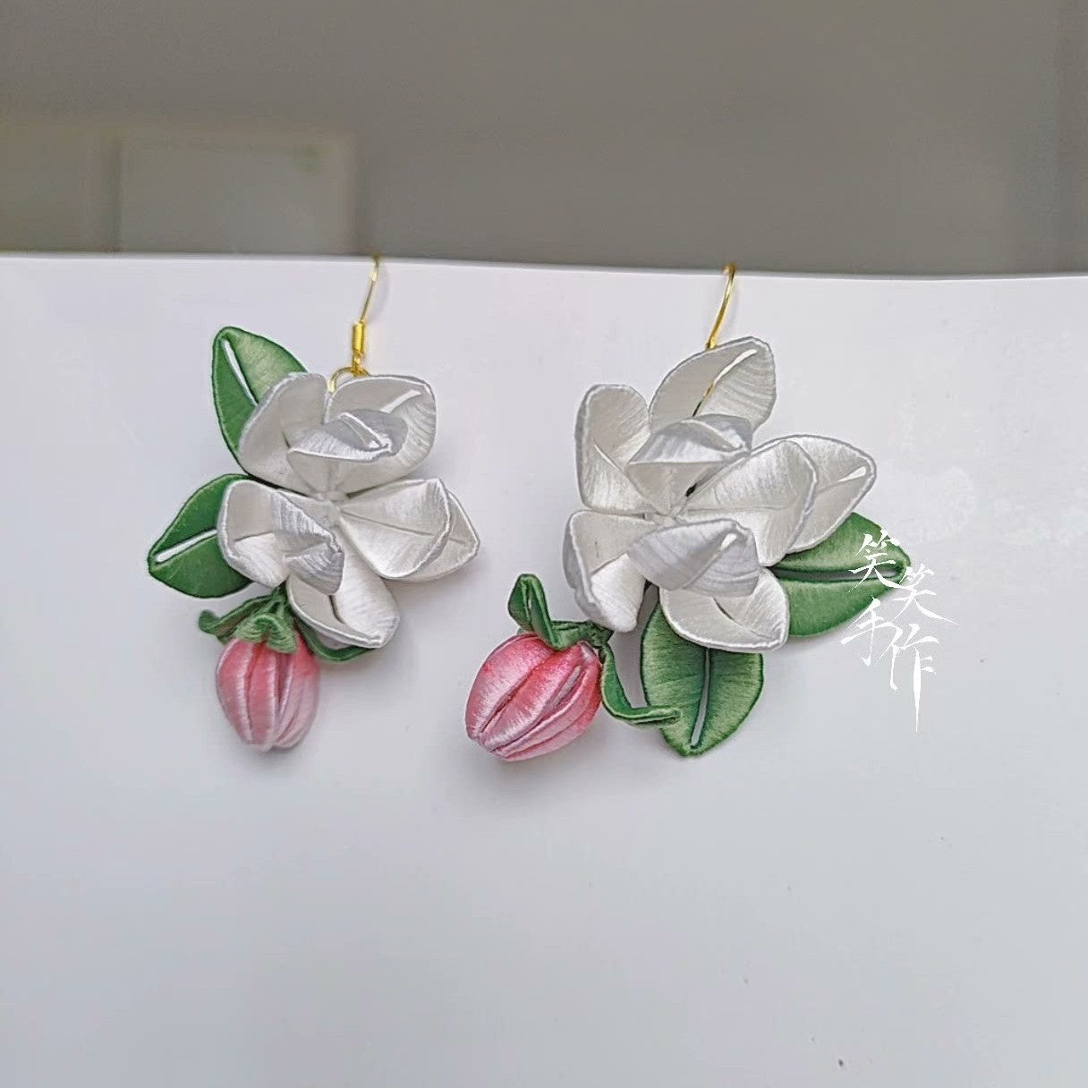 Close-up of the elegant handcrafted white Chanhua flower earrings, highlighting the intricate details of the petals, leaves, and pink buds, showcasing their suitability for daily wear and special occasions.