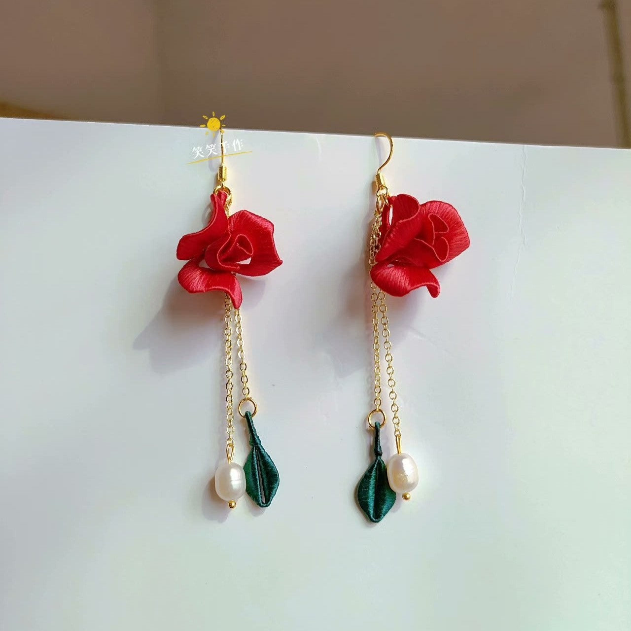 Close-up of handmade Chanhua red rose and green leaf dangle earring with natural freshwater pearl, featuring a 925 silver hook, on a white background.