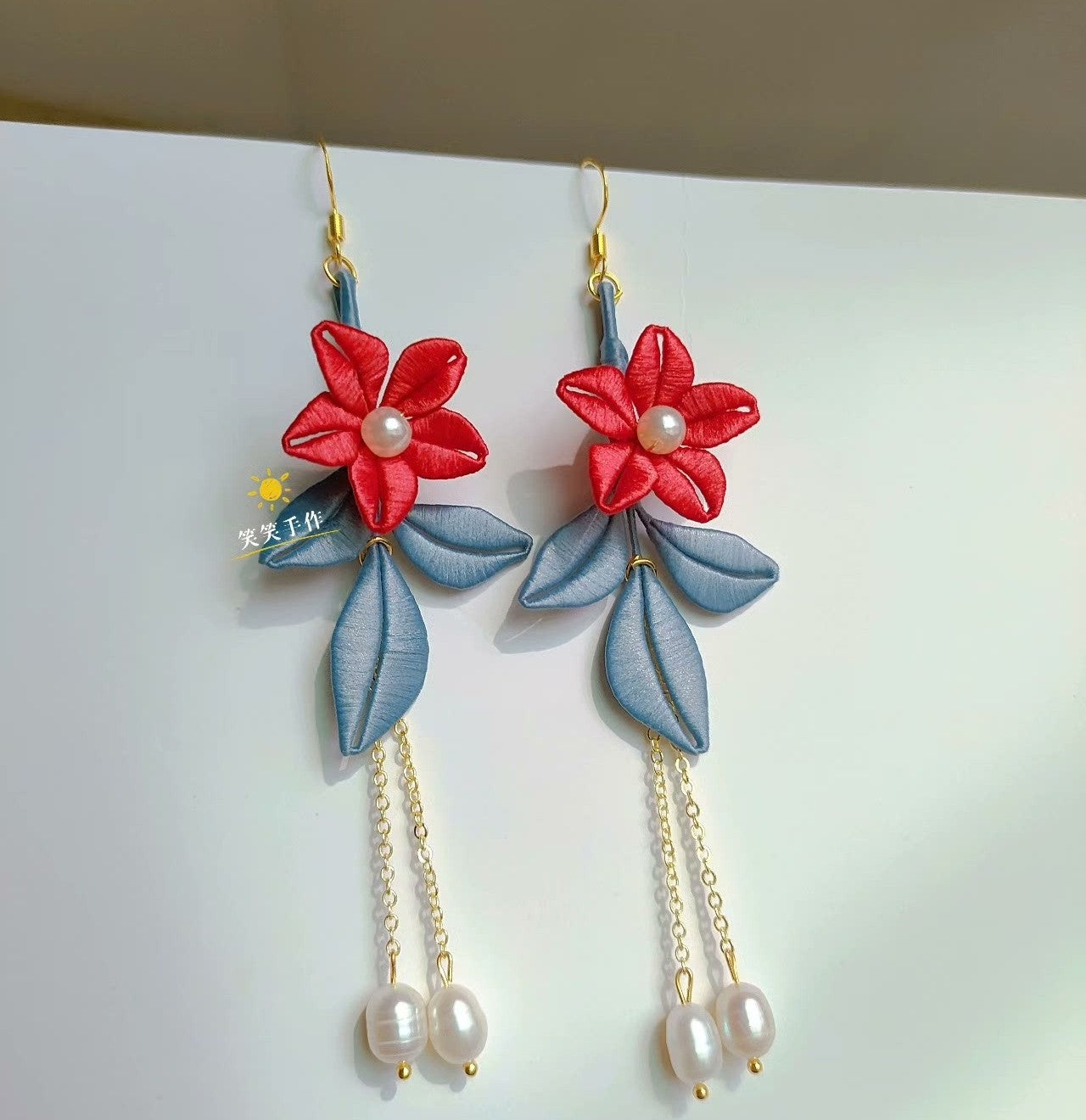 Close-up of a single handcrafted Chanhua earring, showcasing the intricate red fabric flower, blue-grey leaf detail, 925 silver hook, and natural freshwater pearl.