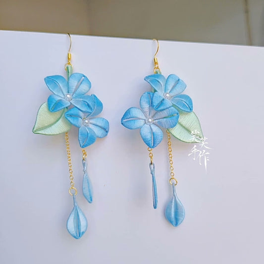 Close-up of a pair of handcrafted blue chanhua flower earrings with green leaves and pearl accents, featuring 925 silver hooks.