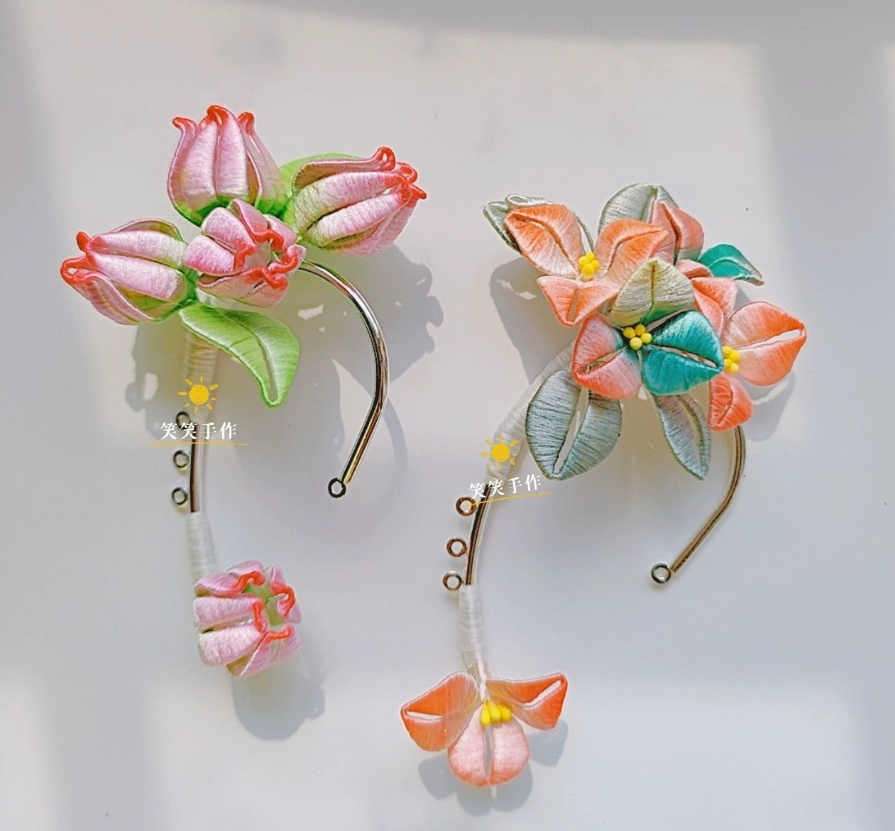 Two handmade Chanhua ear cuffs, one with pink floral buds and the other with open multi-colored flowers, displayed side-by-side on a white surface, highlighting their delicate craftsmanship.