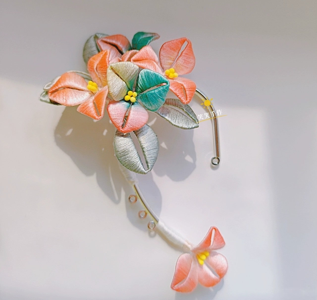 A single pure handmade Chanhua ear cuff with vibrant orange, teal, and grey silk flowers and leaves, showcasing intricate winding technique on a white background.