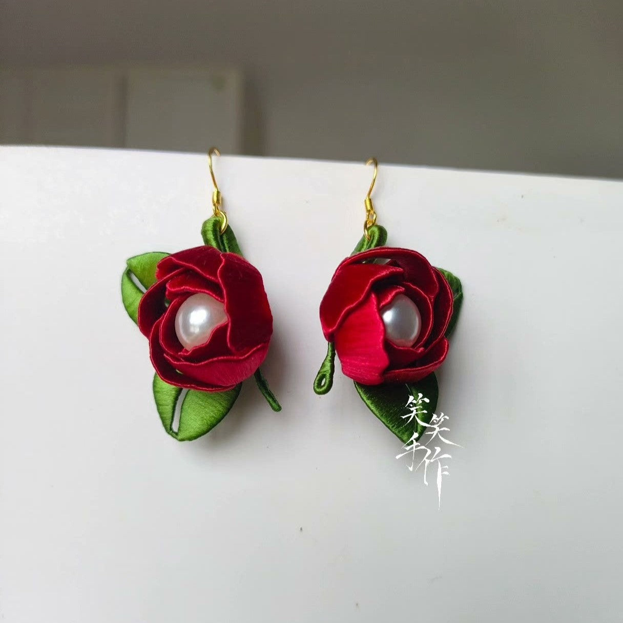 A pair of handcrafted Chanhua red rose and freshwater pearl drop earrings with green leaves, displayed on a white surface.