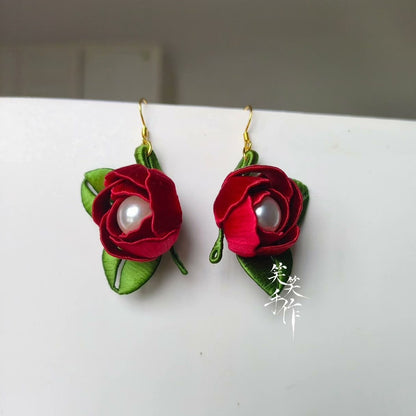 A pair of handcrafted Chanhua red rose and freshwater pearl drop earrings with green leaves, displayed on a white surface.