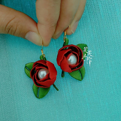 A hand holding up a handcrafted Chanhua rose and pearl earring, showcasing its size and detailed craftsmanship against a blue background.