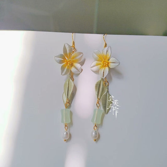 Handmade Chanhua flower earrings with white petals, yellow centers, green leaves, and pearl drops on a white background.