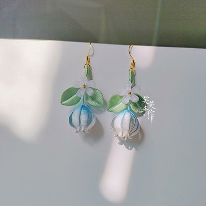 A pair of handmade Chanhua flower and bud dangle earrings with 925 silver hooks, featuring delicate white flowers, green leaves, and blue-tinged buds, presented on a white surface.