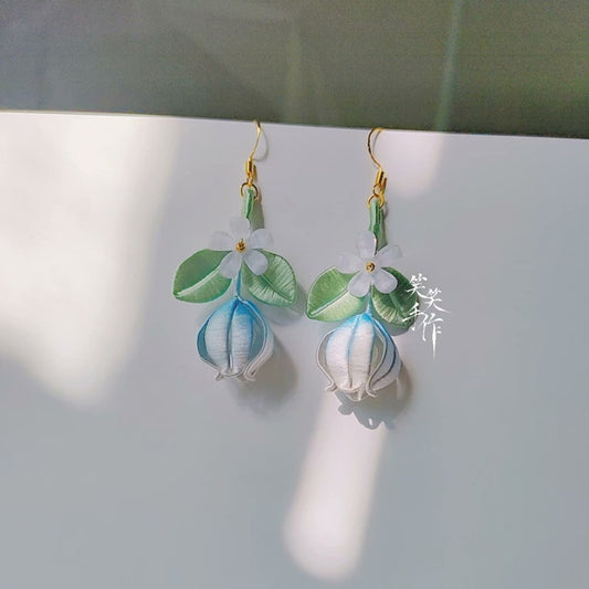 A pair of handmade Chanhua flower and bud dangle earrings with 925 silver hooks, featuring delicate white flowers, green leaves, and blue-tinged buds, presented on a white surface.