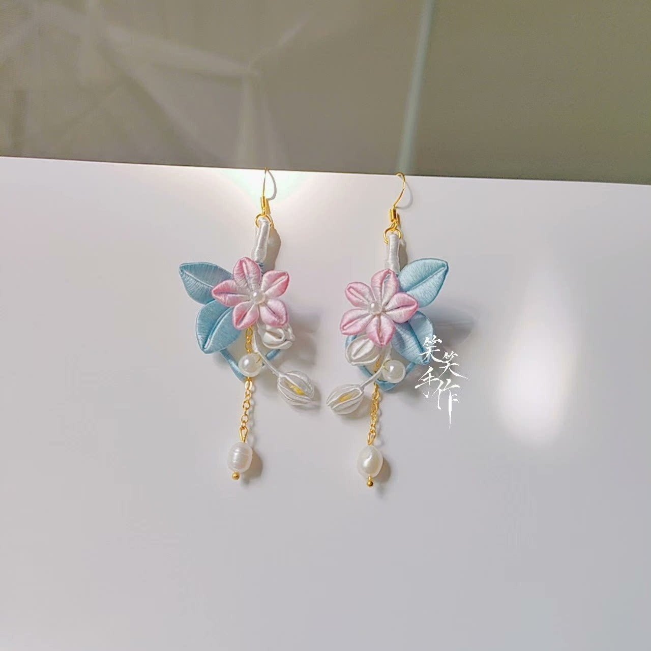 Close-up of a pair of Chanhua earrings featuring intricate fabric flowers, lustrous pearls, and sterling silver ear hooks.