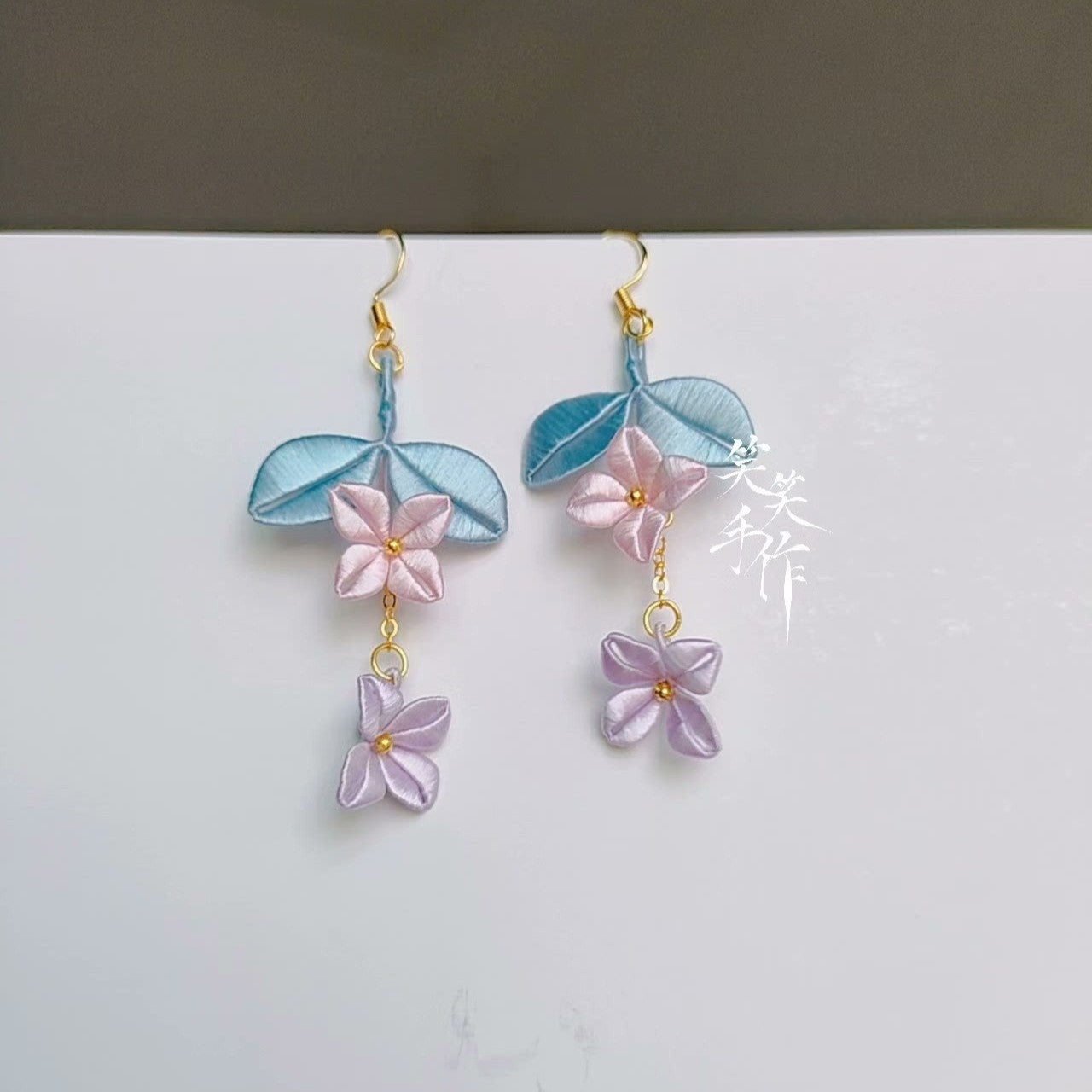 Handmade Chanhua floral dangle earrings with pink and lavender silk petals, blue leaves, and 925 silver hooks, displayed on a white background.