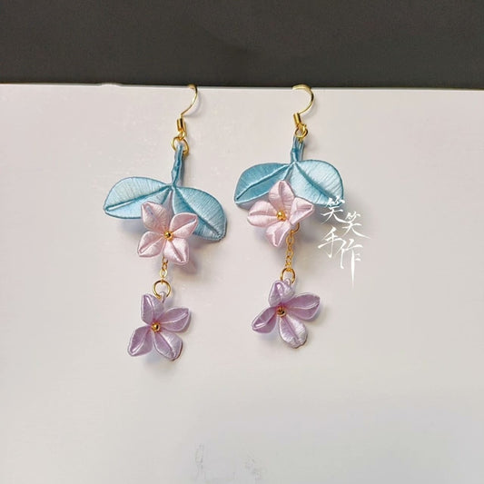 Close-up view of a pair of handcrafted Chanhua earrings, showcasing intricate embroidery details and the delicate color transition of the flowers.