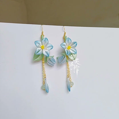 Full view of elegant handmade Chanhua flower earrings featuring intricate silk artistry, blue and green accents, and gold-tone chains with small jade-like beads, suspended for display.