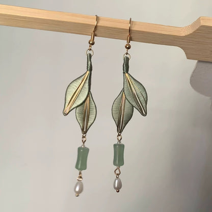 A pair of elegant Chanhua earrings with light green leaves, a translucent bead, and a freshwater pearl, laid on a white surface.