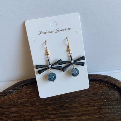 Handmade Chanhua earrings featuring a black ribbon bow and a blue marbled beaded drop, displayed on a white card.