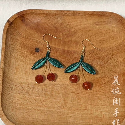 Close-up of a single handmade Chanhua cherry earring, showing the intricate details of the silk leaf and the translucent red bead.