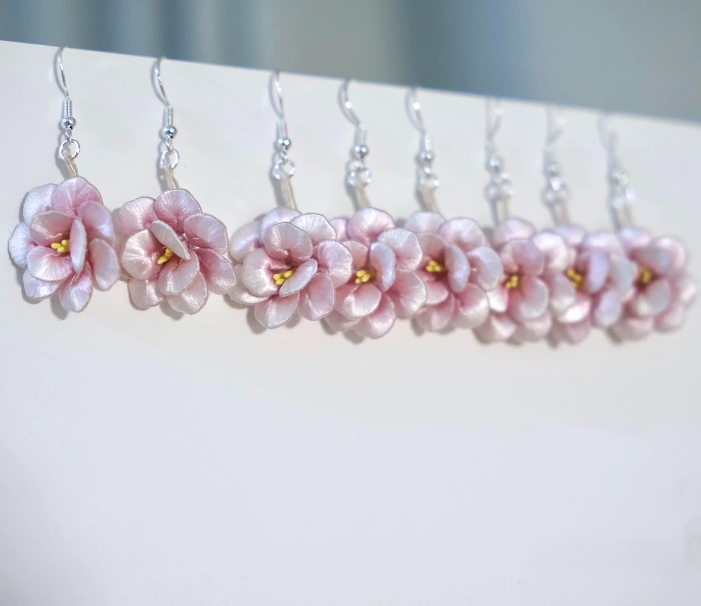 A row of handmade pink camellia flower earrings with 925 sterling silver hooks, hanging neatly against a white background.