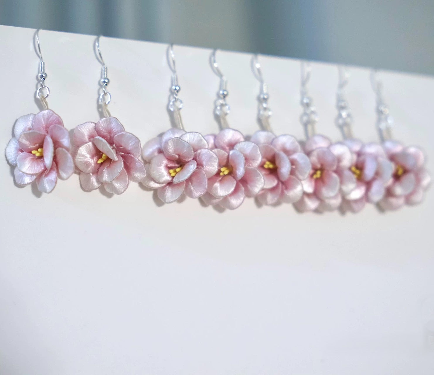A row of handmade pink camellia flower earrings with 925 sterling silver hooks, hanging neatly against a white background.