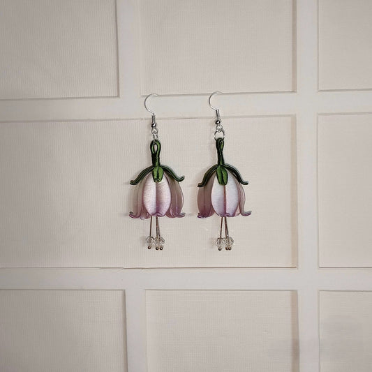 A pair of handmade Chanhua flower dangle earrings on a white textured background. The earrings feature light purple petals and a green stem, with small crystal beads at the bottom.