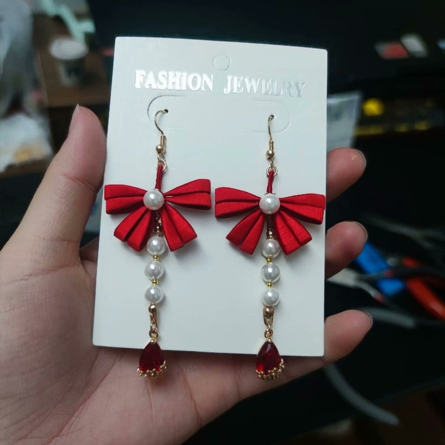 Handmade Chanhua earrings with red bow, white pearls, and red teardrop crystal, on a white display card.