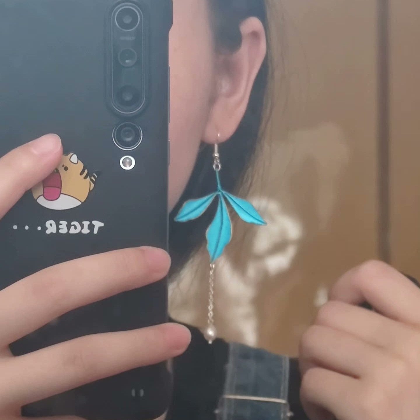 Close-up of a person wearing a single handmade blue Chanhua leaf dangle earring with a freshwater pearl and a 925 silver hook.